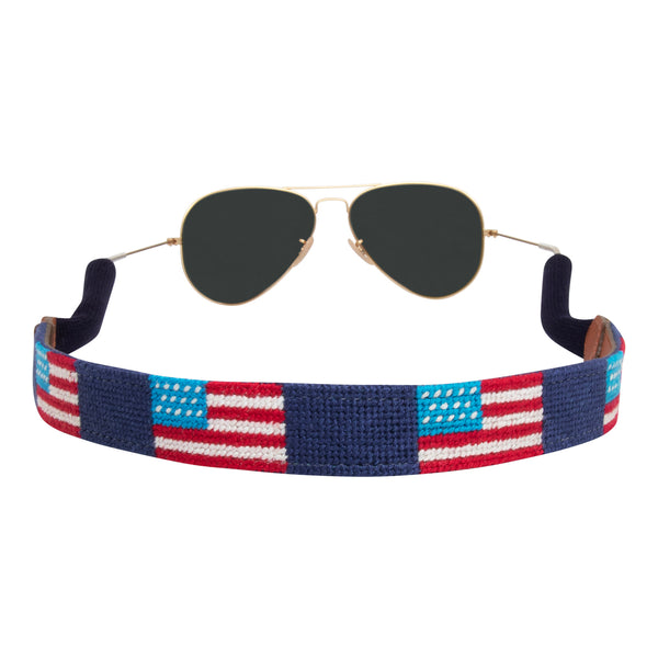 Side view of handstitched American Flag needlepoint sunglass strap showing American Flags against a navy blue background with sturdy cotton covered silicone ear connectors and a soft leather backing