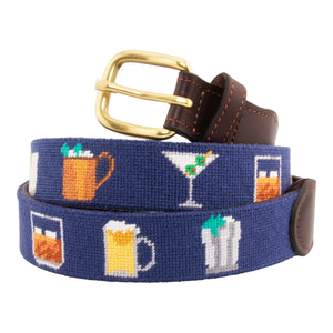 Cocktail Needlepoint Belt with navy blue background showing a repeating pattern of popular cocktails such as a martini, bourbon on the rocks, glass of wine, beer, mint julep around the belt. Belt has a brass buckle and full grain leather backing and strap.