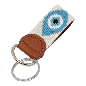 Hand-stitched evil eye needlepoint keychain showing an evil eye on both sides against a stone colored background and leather backing.  Stainless steel D-ring and keyring.