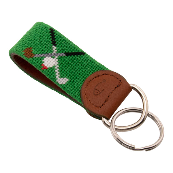 Hand-stitched golfing themed needlepoint keychain showing crossed golf clubs on both sides against a green background and leather backing.  Stainless steel D-ring and keyring.