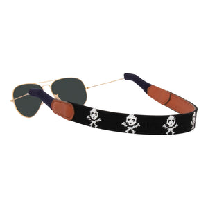 jolly roger needlepoint sunglass strap showing white skull and crossbones pattern against a black background with sturdy cotton covered silicone ear connectors and a soft leather backing