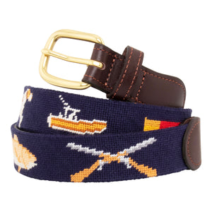 Sportsman Needlepoint Belt with navy blue colored background showing outdoor sporting themed images of a pointer dog, crossed shotguns, shotgun shell, fly fishing rod, redfish, fishing boat, flying duck and dove.  Belt has brass buckle and full-grain leather backing.