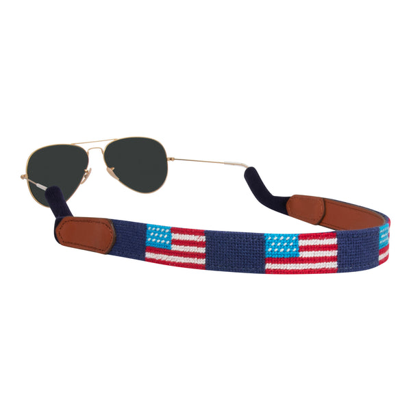 Handstitched American Flag needlepoint sunglass strap showing American Flags against a navy blue background with sturdy cotton covered silicone ear connectors and a soft leather backing