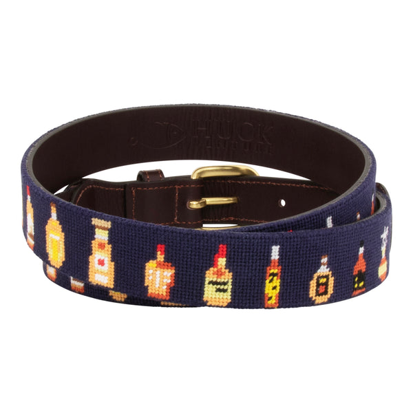 Bourbon Bottle Needlepoint Belt with navy blue background showing a repeating pattern of popularbourbon bottles around the belt. Belt has a brass buckle and full grain leather backing and strap.
