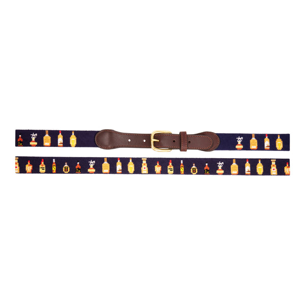 Bourbon Bottle Needlepoint Belt with navy blue background showing a repeating pattern of popularbourbon bottles around the belt. Belt has a brass buckle and full grain leather backing and strap.