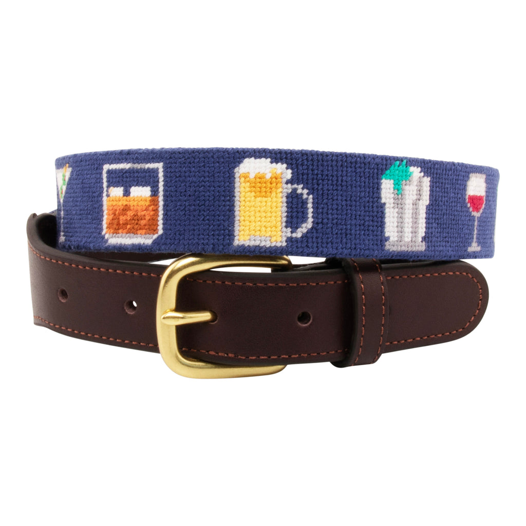 Cocktail Needlepoint Belt with navy blue background showing a repeating pattern of popular cocktails such as a martini, bourbon on the rocks, glass of wine, beer, mint julep around the belt. Belt has a brass buckle and full grain leather backing and strap.