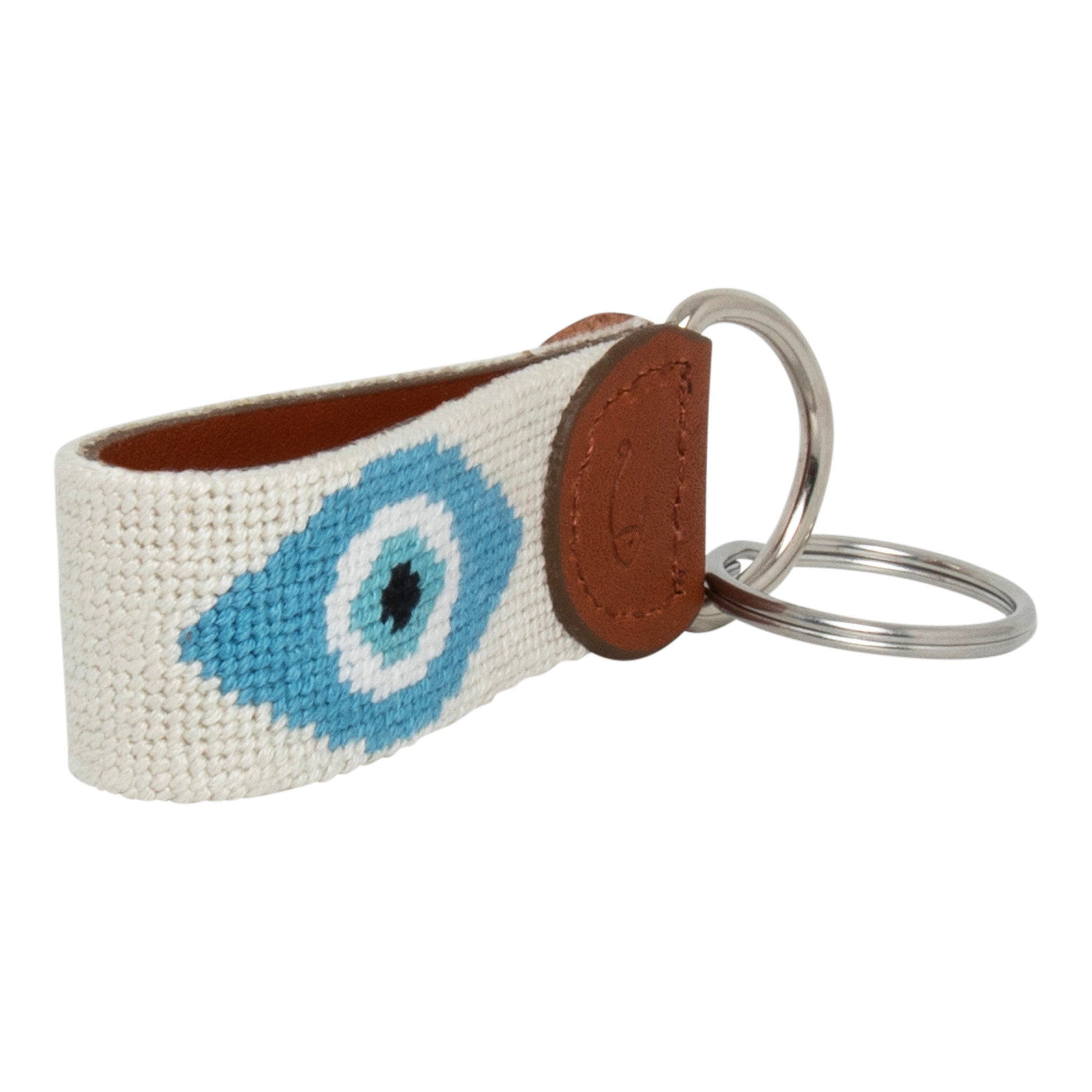 Hand-stitched evil eye needlepoint keychain showing an evil eye on both sides against a stone colored background and leather backing.  Stainless steel D-ring and keyring.
