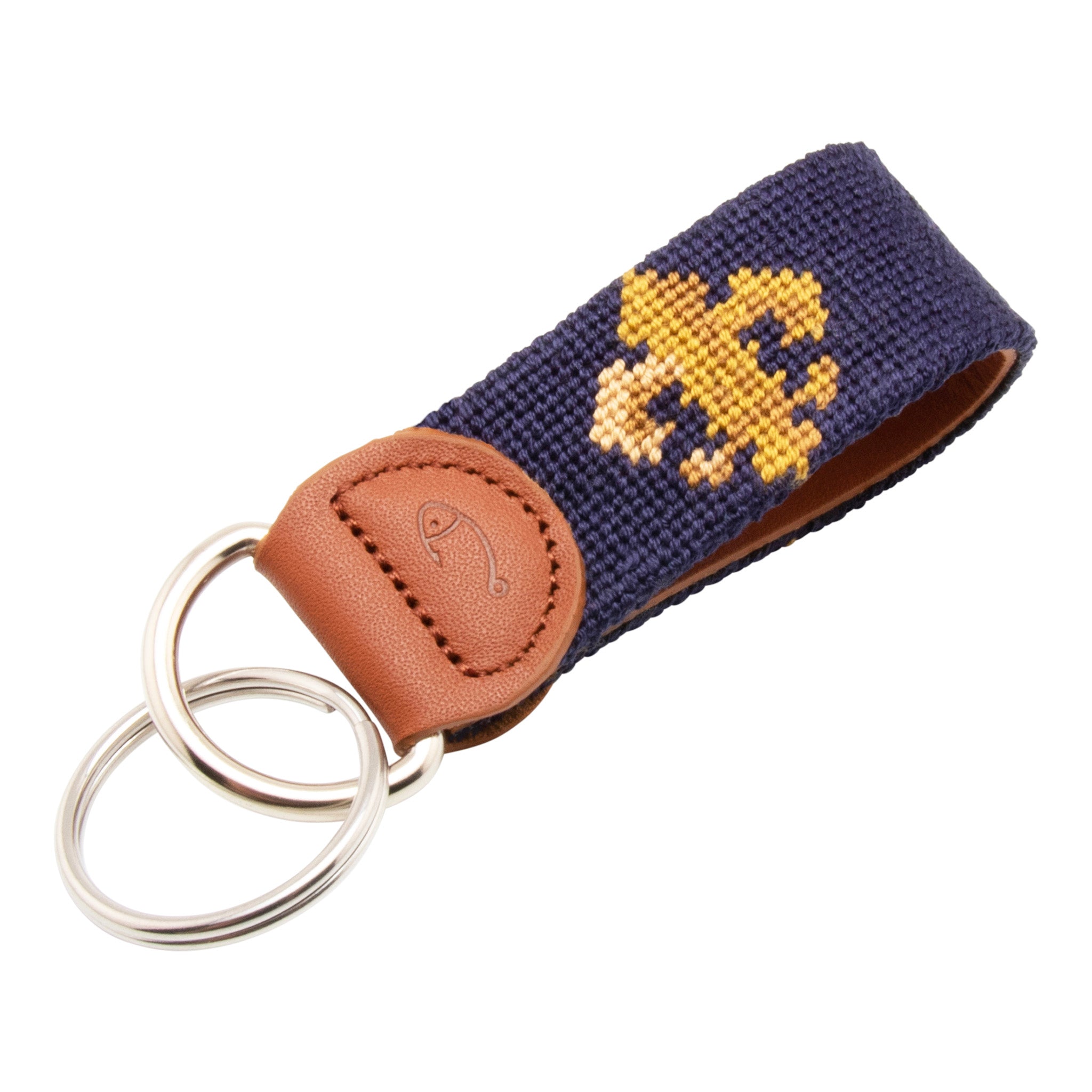 A navy blue key fob with a fleur-de-lis pattern and a brown leather section with a stainless steel keyring.