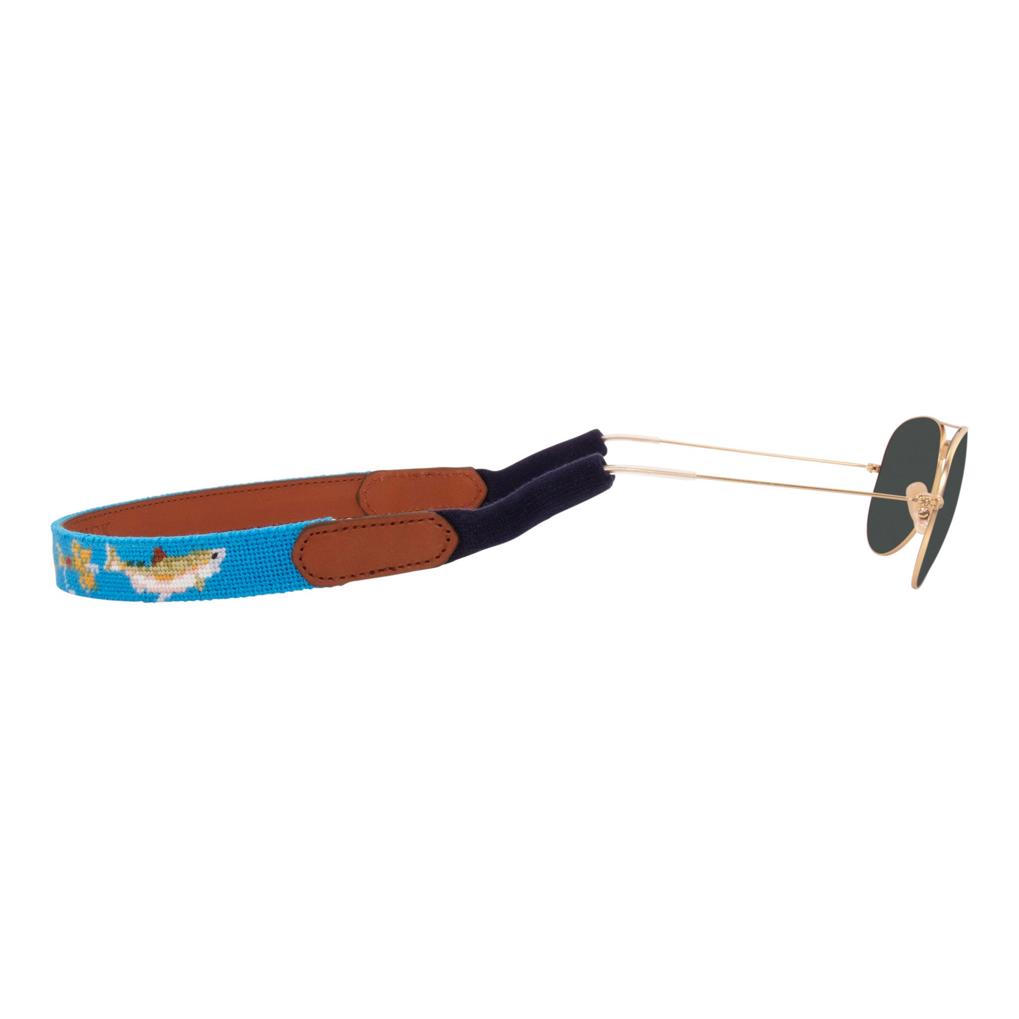 Fly Fishing Needlepoint Sunglass Strap with light blue background showing a fly-fishing themed pattern of rainbow trout, salmon, fly rods and reels, dry flies, nymph patterns, and cutthroat.  Sunglass straps have a full grain leather backing and secure cotton wrapped ear piece connectors for a secure grip. 