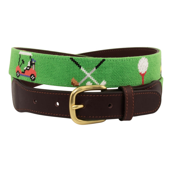 Golfing Needlepoint Belt with light green background showing a repeating pattern of teed gold ball, crossed gold clubs, and colorful golf carts. Belt has a brass buckle and full grain leather backing and strap.