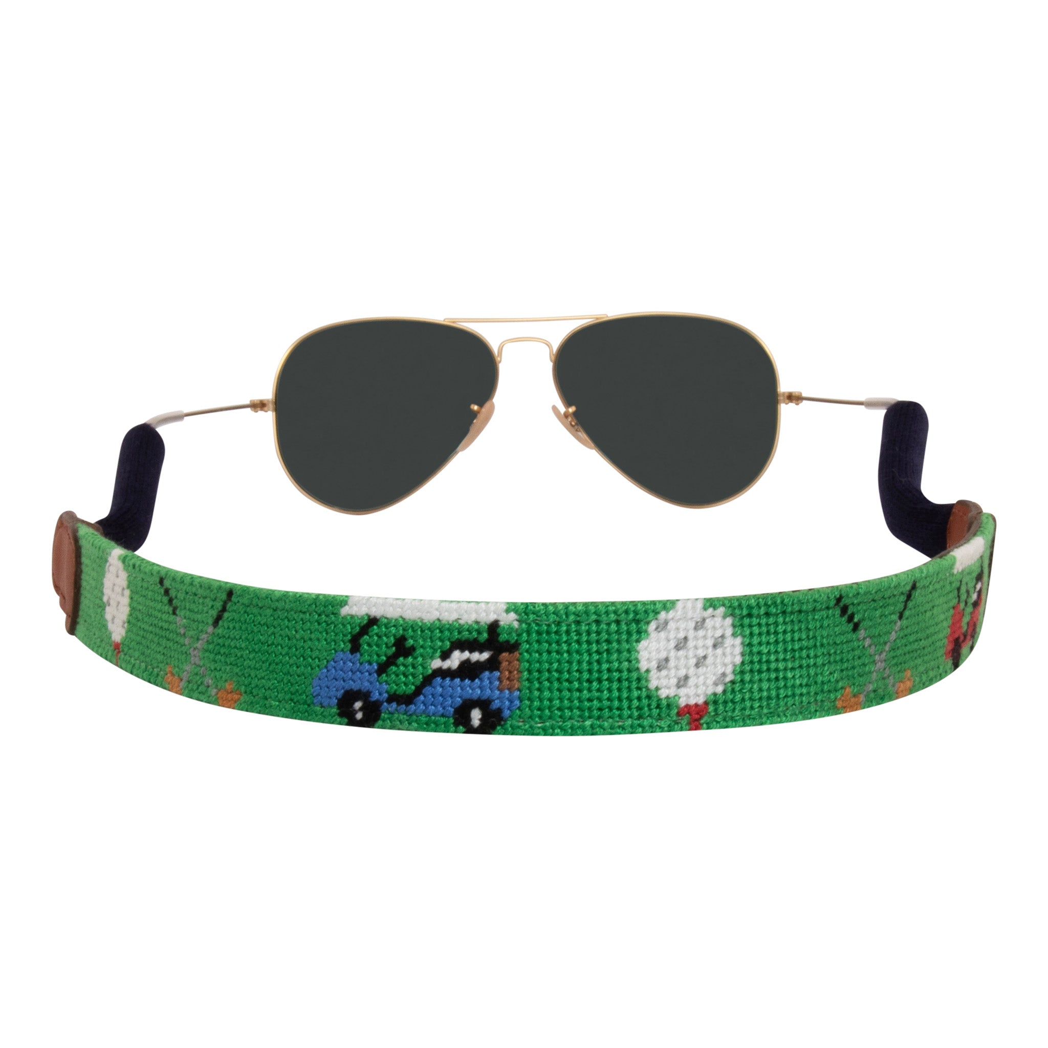 Back view of golfing theme handmade needlepoint sunglass strap showing golf carts golf clubs golf balls against a green background with sturdy cotton covered silicone ear connectors and a soft leather backing