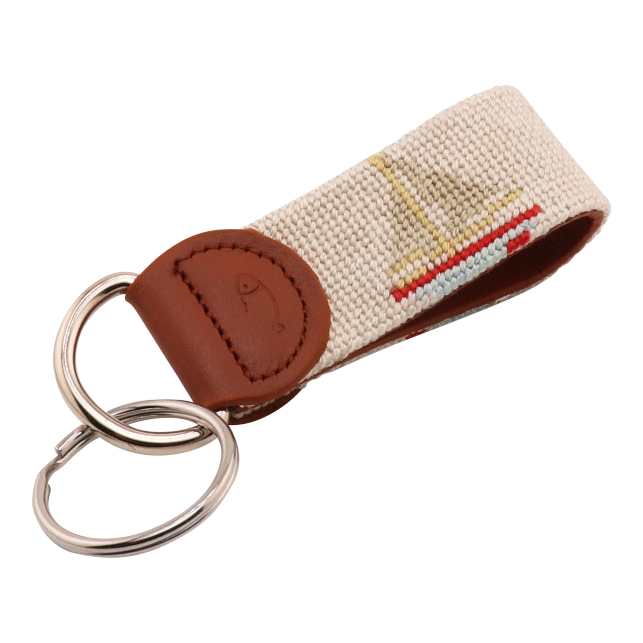 A beige and brown sailing needlepoint key fob with a needlepoint design featuring a sailboat, backed with full-grain leather, and secured with a chrome key ring.
