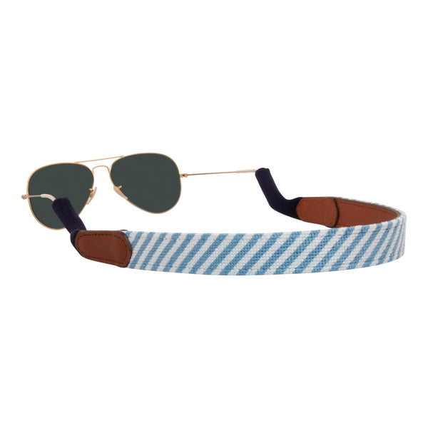 handmade seersucker needlepoint sunglass strap showing a blue and white seersucker classic pattern with sturdy cotton covered silicone ear connectors and a soft leather backing