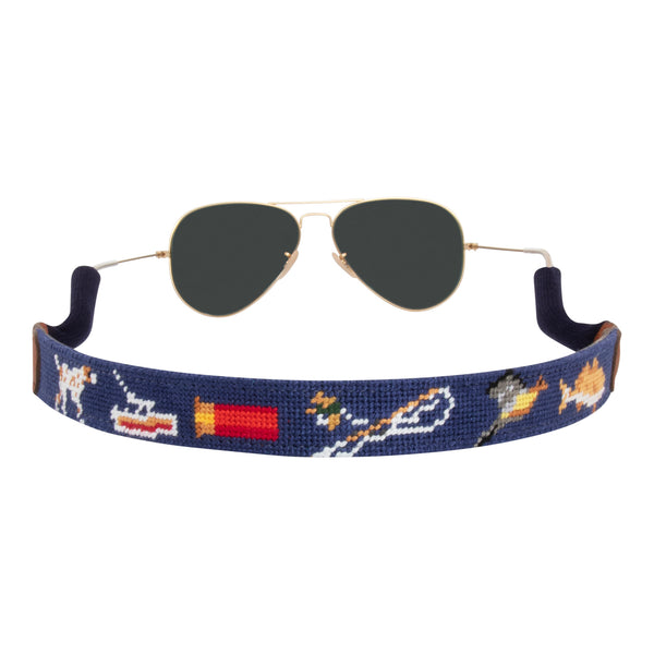 Back view southern sportsman themed needlepoint sunglass strap showing shotgun dove pointer dog fish patterns against a navy blue background with sturdy cotton covered silicone ear connectors and a soft leather backing